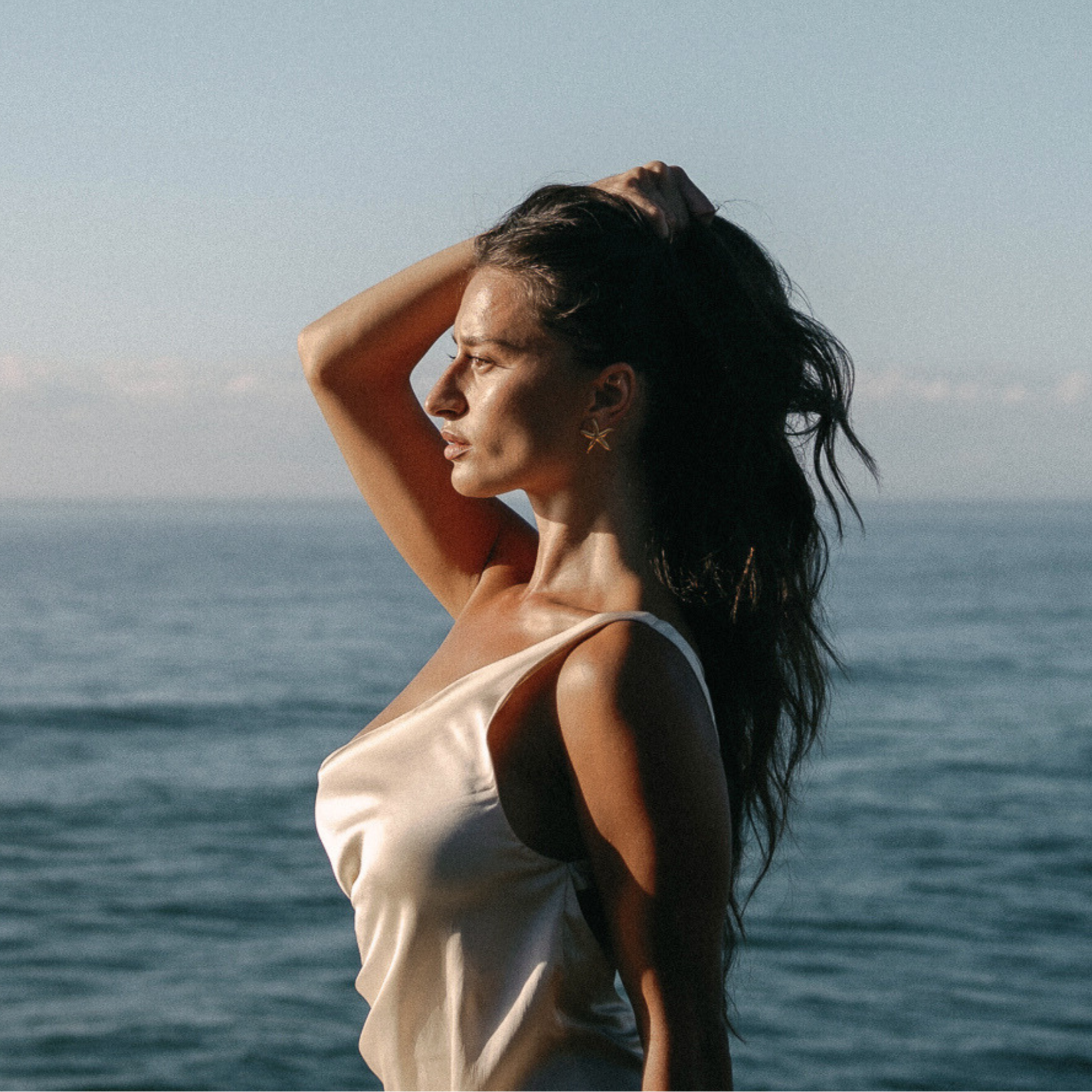 Woman standing by the ocean with a clear sky